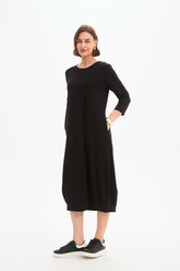 Black jersey midi dress featuring a round neckline, 3/4 sleeves, side pockets, relaxed cocoon silhouette, and banded hem.
