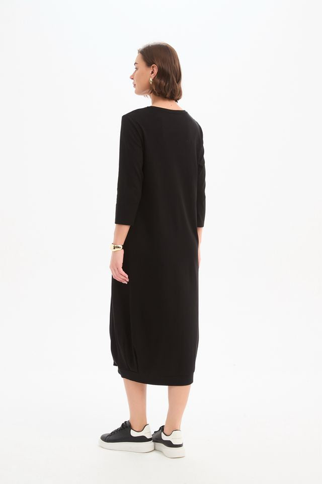 Black jersey midi dress featuring a round neckline, 3/4 sleeves, side pockets, relaxed cocoon silhouette, and banded hem.