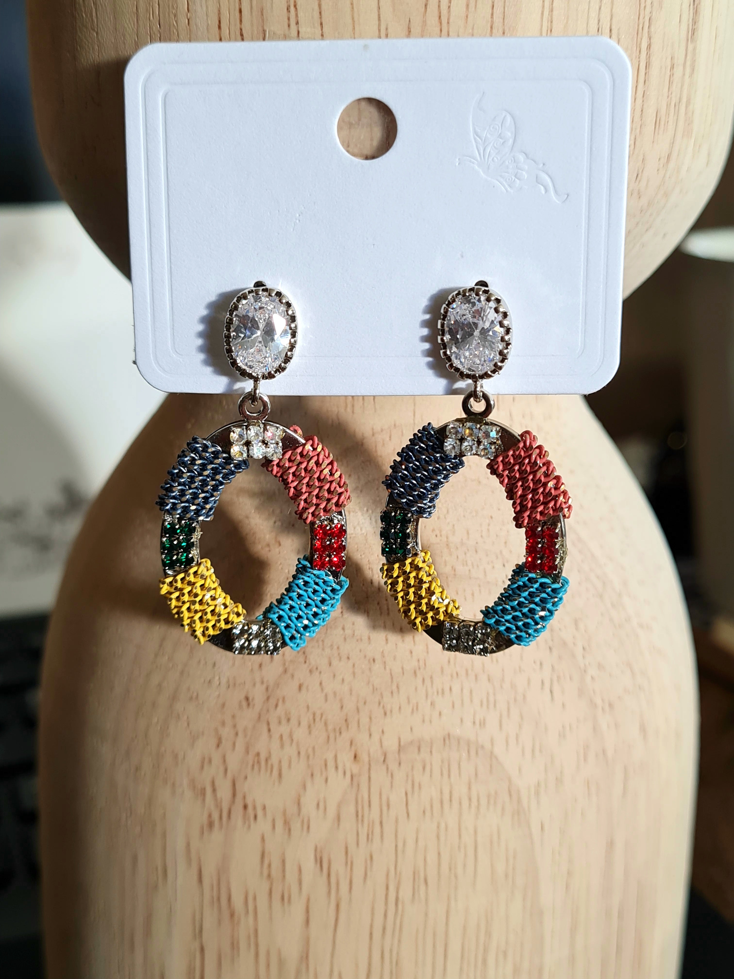 "Handmade oval-shaped earrings from Linens & Treasures, featuring intricate beadwork and crystals, available in two color variations: this one with bold reds, yellow, teal, and black, and another in subtle tones of black, green, and beige."