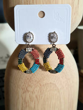 "Handmade oval-shaped earrings from Linens & Treasures, featuring intricate beadwork and crystals, available in two color variations: this one with bold reds, yellow, teal, and black, and another in subtle tones of black, green, and beige."