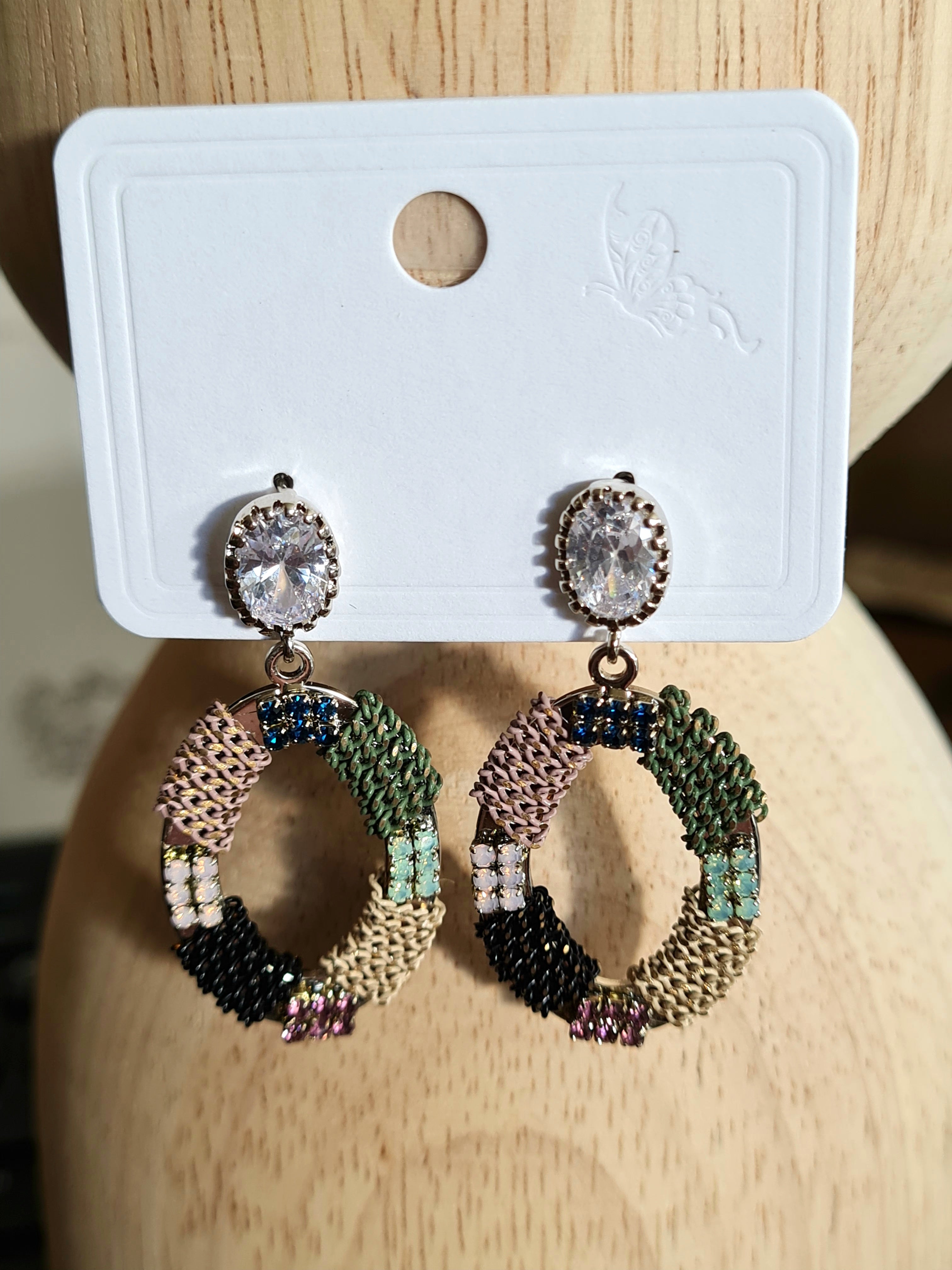 "Handmade oval-shaped earrings from Linens & Treasures, featuring intricate beadwork and crystals, available in two color variations: one with bold reds, yellow, teal, and black, and this one in subtle tones of black, green, and beige."