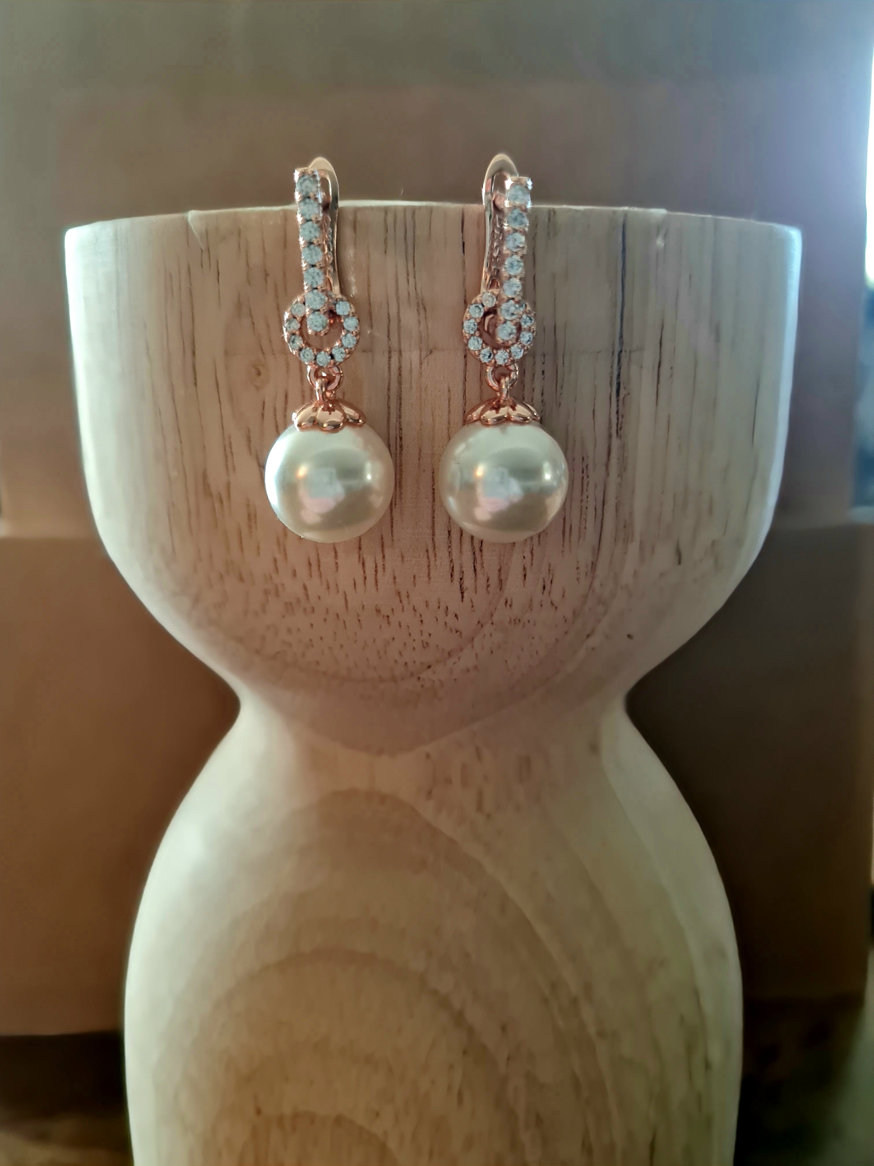 Pair of pearl earrings on a wooden stand.