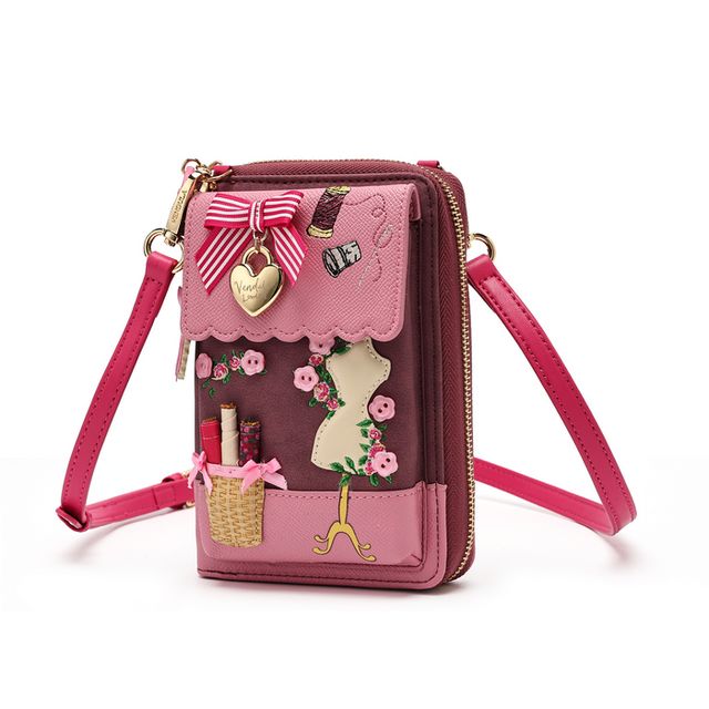 Vendula London X Pink Ribbon Sewing Box Scrapbook Bree Phone Pouch in printed and embossed vegan leather, featuring embroidered and appliqué sewing-themed artwork with ribbons, roses and haberdashery details. Includes a front phone pocket, magnetic flap closure, ziparound main compartment, multiple internal pockets, mirror and adjustable detachable crossbody strap.