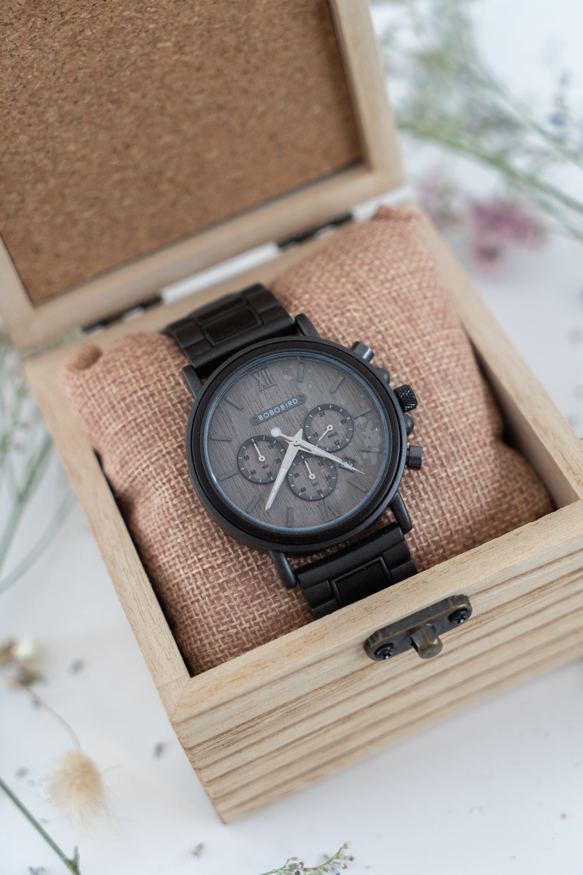 A dark grey analog watch with a metal strap and a woodgrain center face, presented in a wooden box. Check out our Bobo Bird Watch range at Linens & Treasures