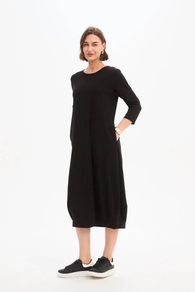 Black jersey midi dress featuring a round neckline, 3/4 sleeves, side pockets, relaxed cocoon silhouette, and banded hem.