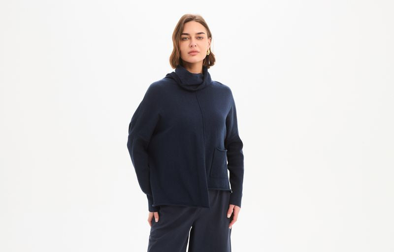 Tirelli Roll Hem Pocket Knit in Navy featuring a relaxed oversized fit, rolled cowl neckline, ribbed sleeves, front patch pocket, exposed centre seam, and asymmetrical roll hem in a classic deep navy knit.