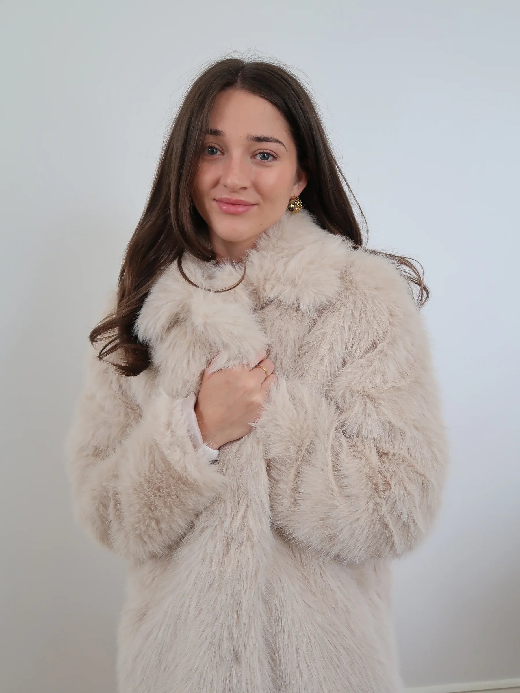 Beige long faux fur coat with soft plush texture, classic collar, and two-button closure in an elegant longline style.