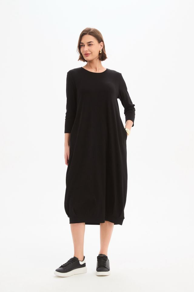 Black jersey midi dress featuring a round neckline, 3/4 sleeves, side pockets, relaxed cocoon silhouette, and banded hem.